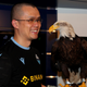Binance CEO Chengpeng Zhao wearing a Binance logo on his shirt, holding an eagle.
